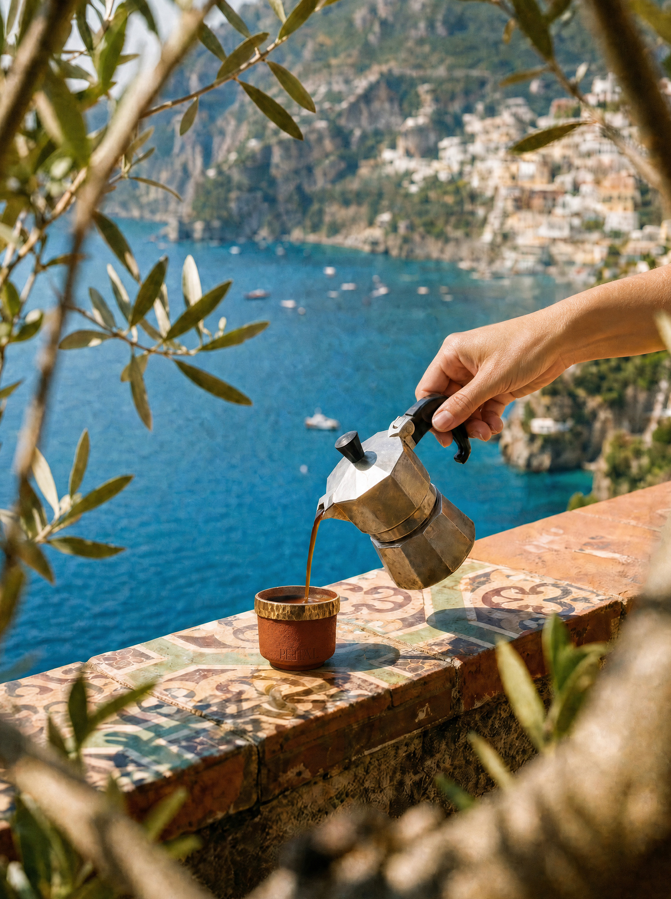 Moka pot pouring into PEETAL on mosaic tile ledge, Positano coast behind
